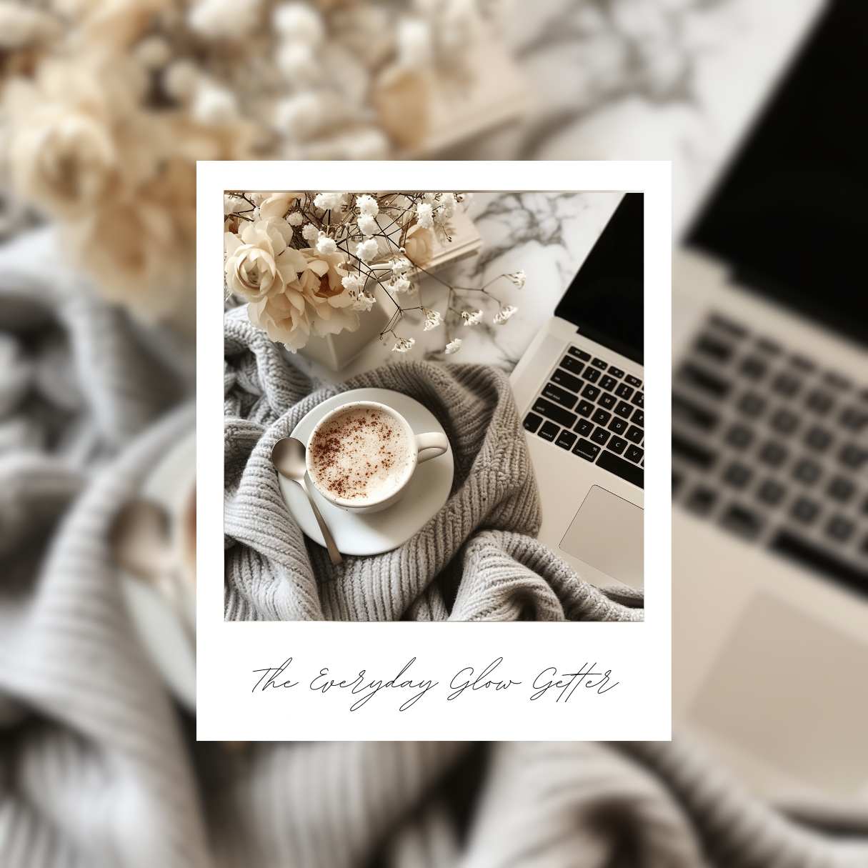 A top down view of a cappuccino, a soft grey blanket, a laptop and a bunch of white flowers 
